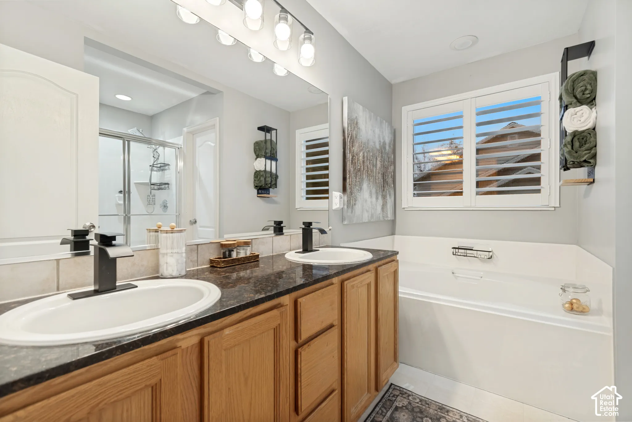 Dual-sink vanity with dark stone-finish countertop, matte black fixtures, full-width mirror, and built-in soaking tub