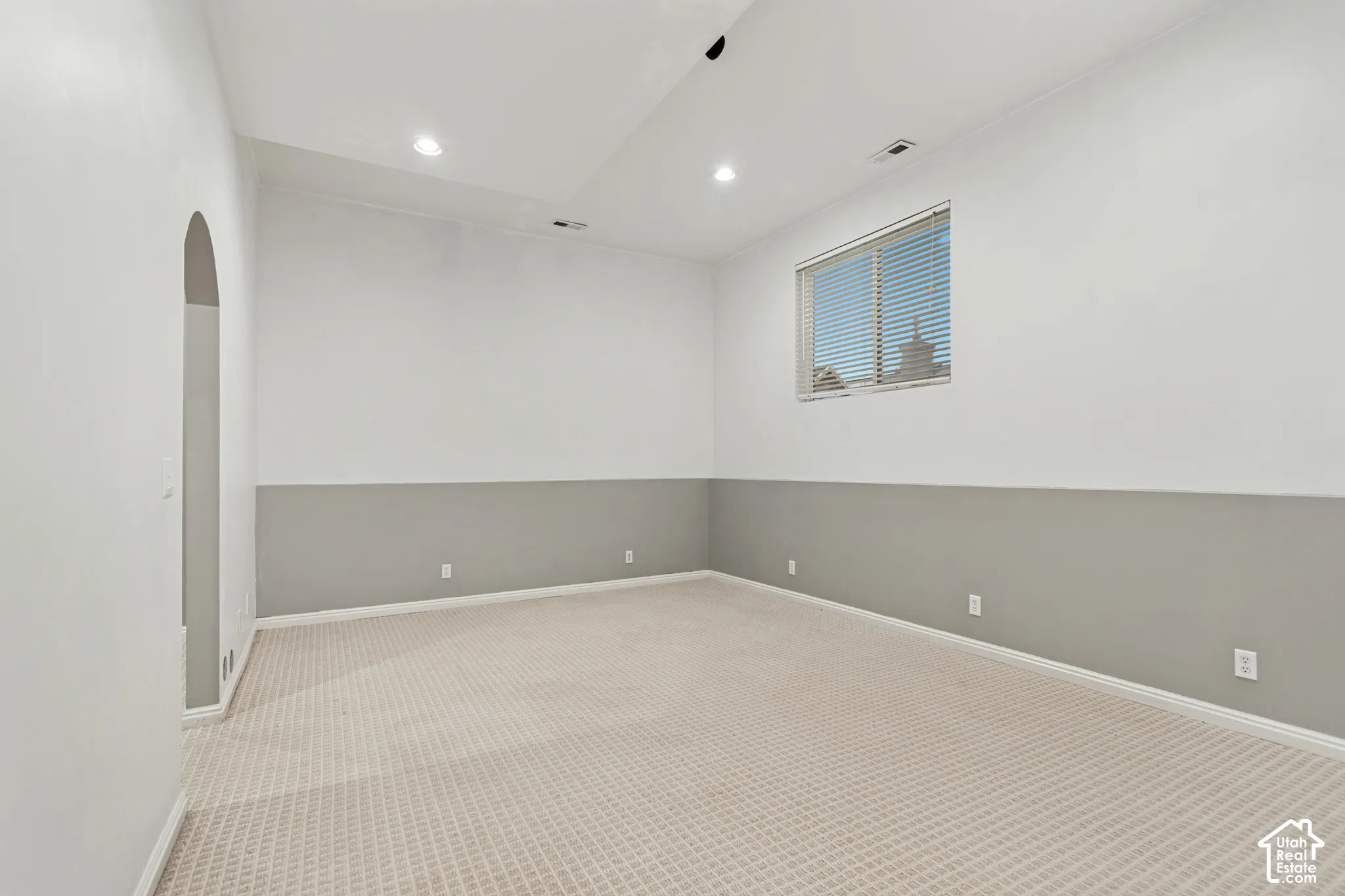 Interior space featuring recessed lighting, high ceilings, neutral-toned wall-to-wall carpeting, two-toned wall paint, and an arched doorway