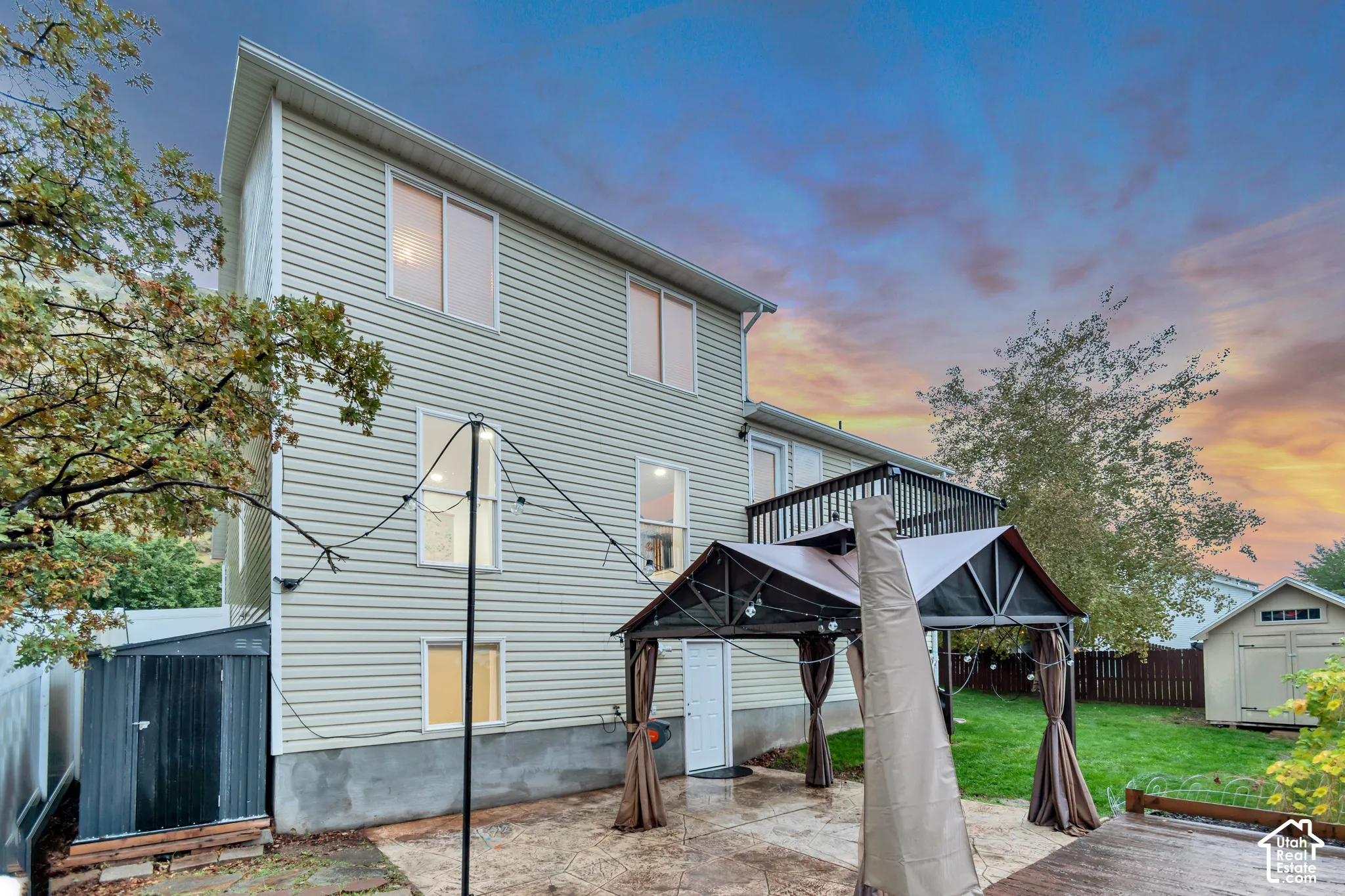 Multi-level home exterior featuring horizontal siding, a stamped concrete patio, an elevated balcony with a metal railing, and a detached storage structure