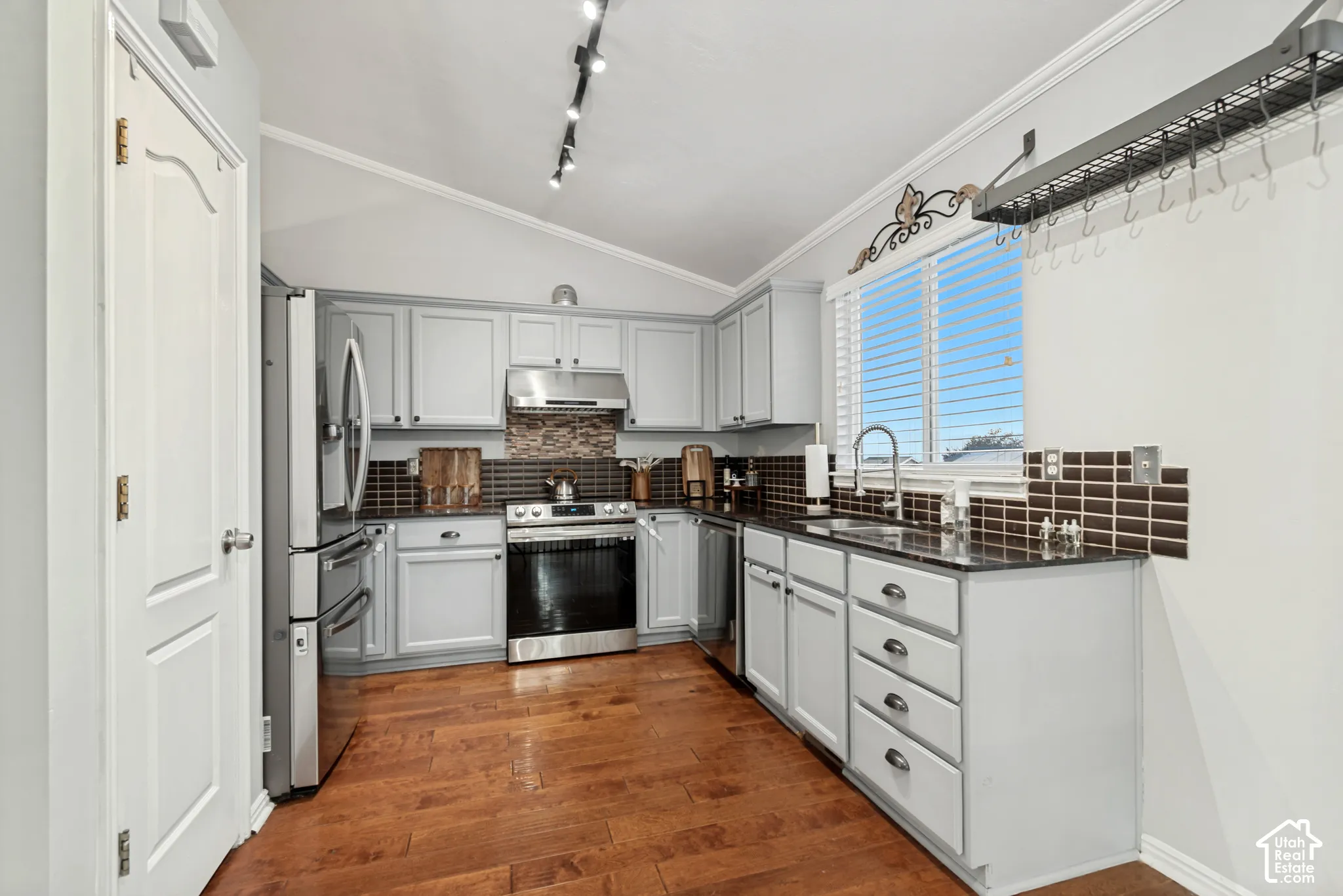 Kitchen featuring wood-finish flooring, light grey cabinetry, dark tile backsplash, stainless steel appliances, and track lighting