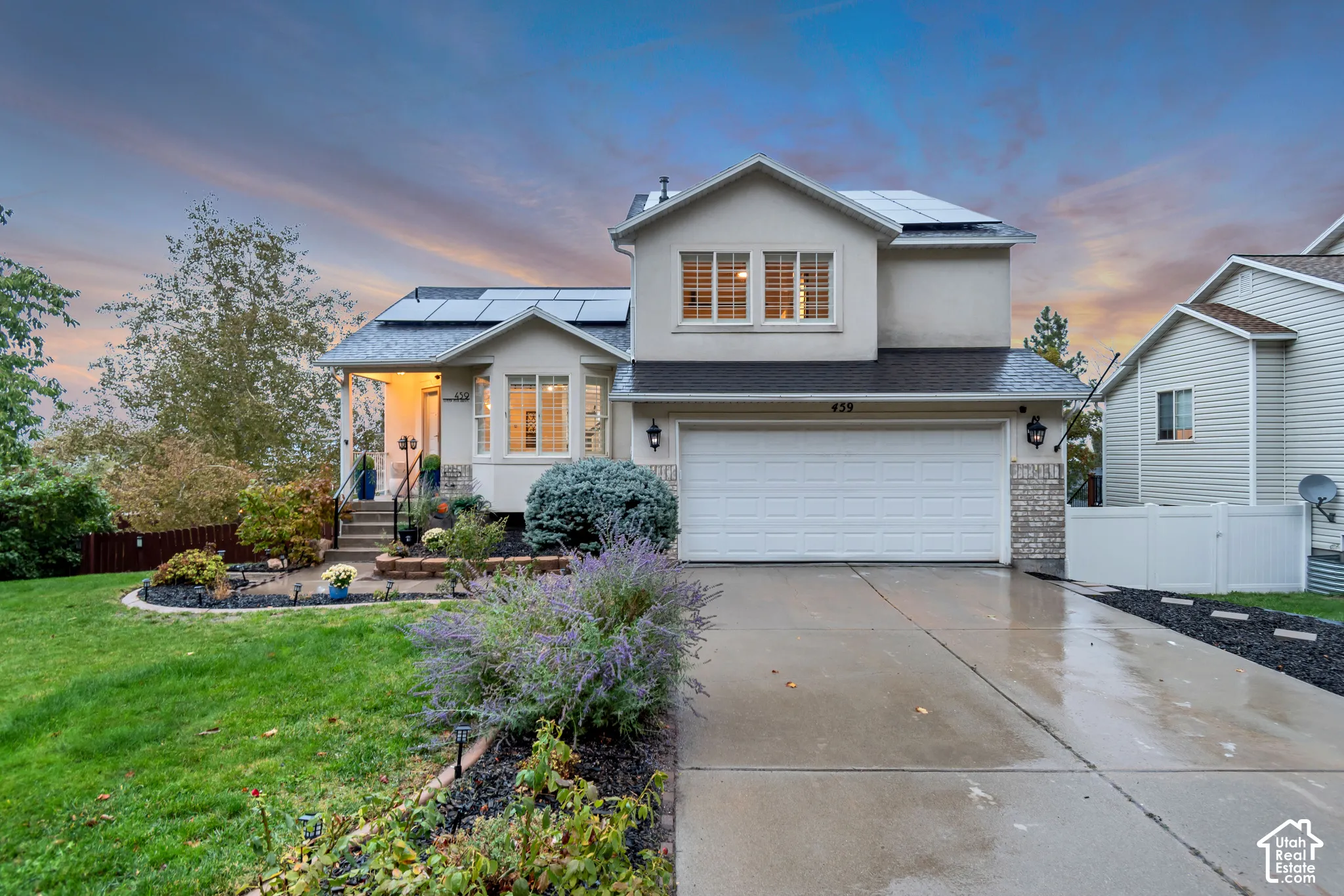 Two-story residence featuring a multi-gabled exterior, concrete driveway, stone facade accents, roof-mounted solar panels, and landscaped front grounds