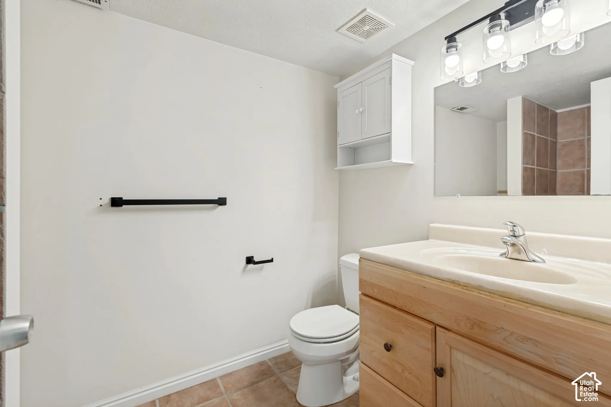 Bathroom featuring a wood-finish vanity with an integrated sink, matte black hardware, wall-mounted cabinetry, and tile flooring