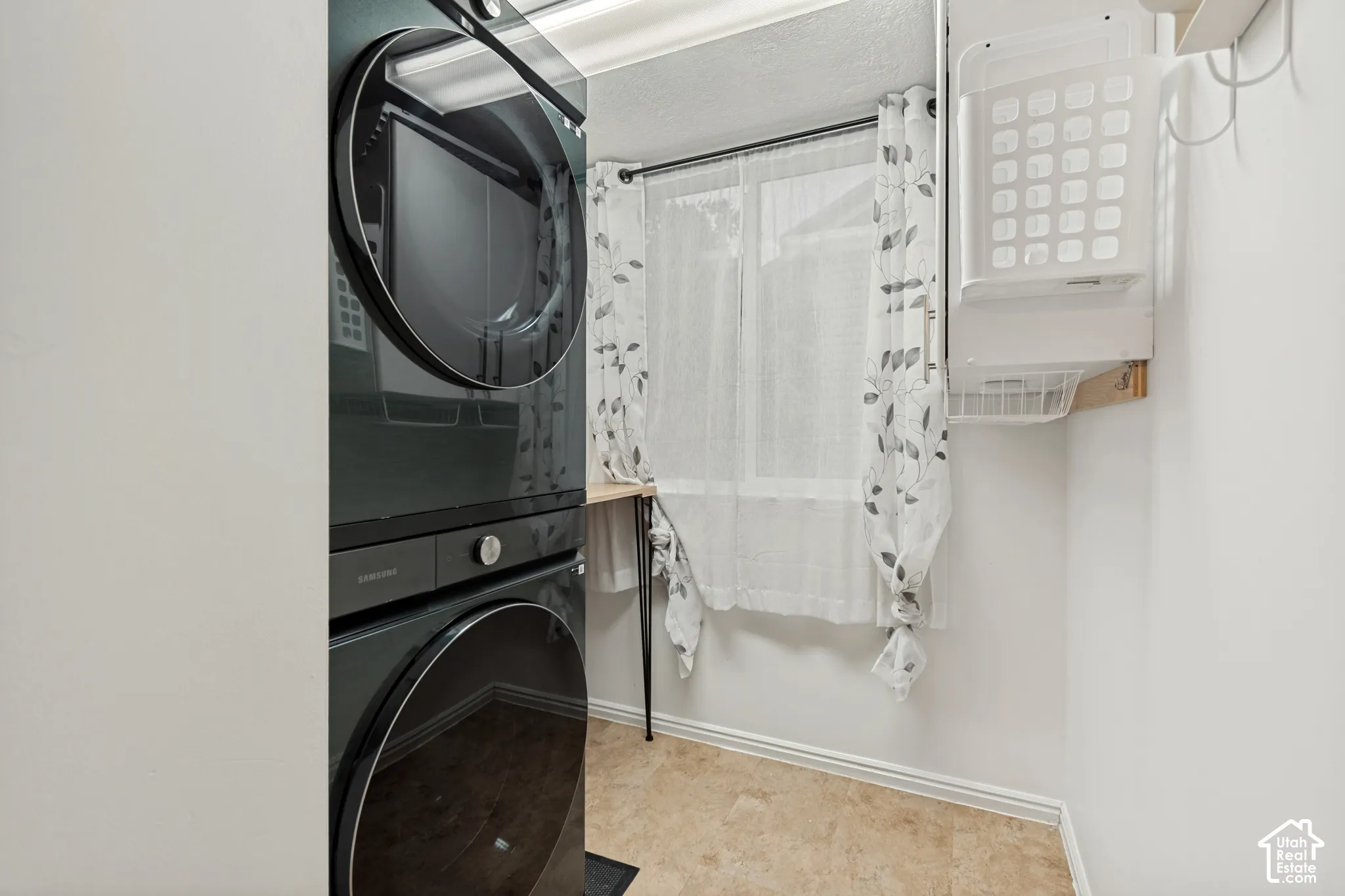 Laundry area featuring a stacked washer and dryer, tile flooring, window, and wood-surface counter