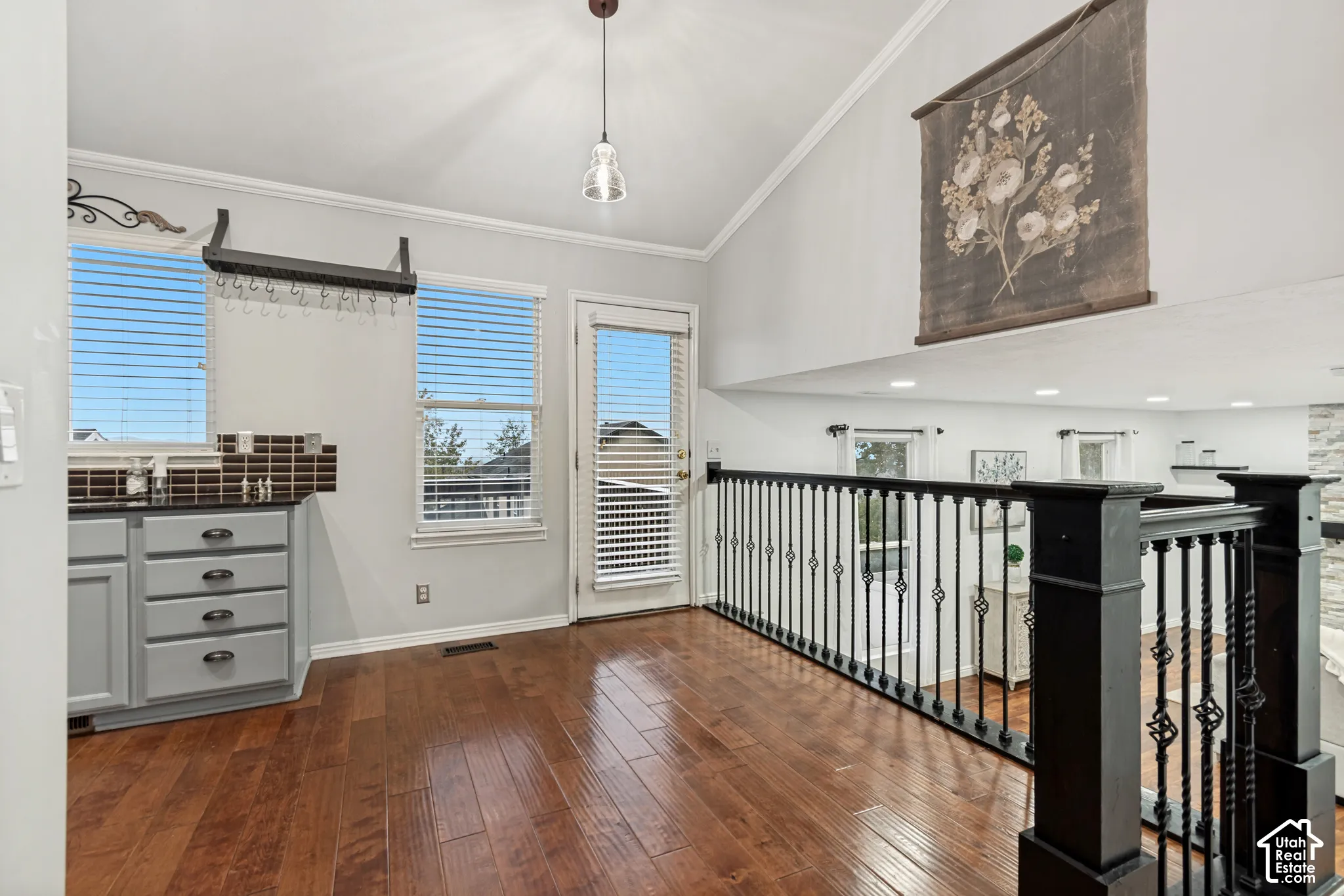 Vaulted ceilings, wood-finish flooring, built-in cabinetry with dark stone surfacing, and decorative iron railings