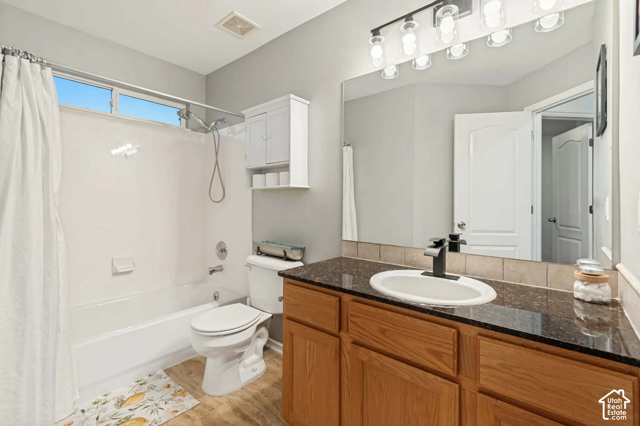 Bathroom featuring a wood-finish vanity with a dark stone countertop, an integrated oval sink with a matte black faucet, a full-width mirror, and a tub-shower combination with tile surround