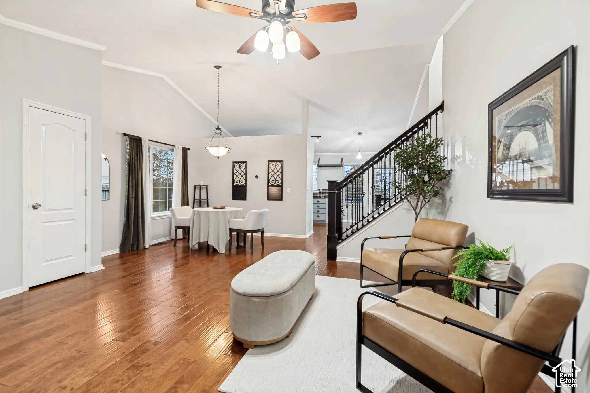 Open-concept interior featuring vaulted ceilings, wood-finish flooring, a metal-railed staircase, and decorative pendant and ceiling fan lighting