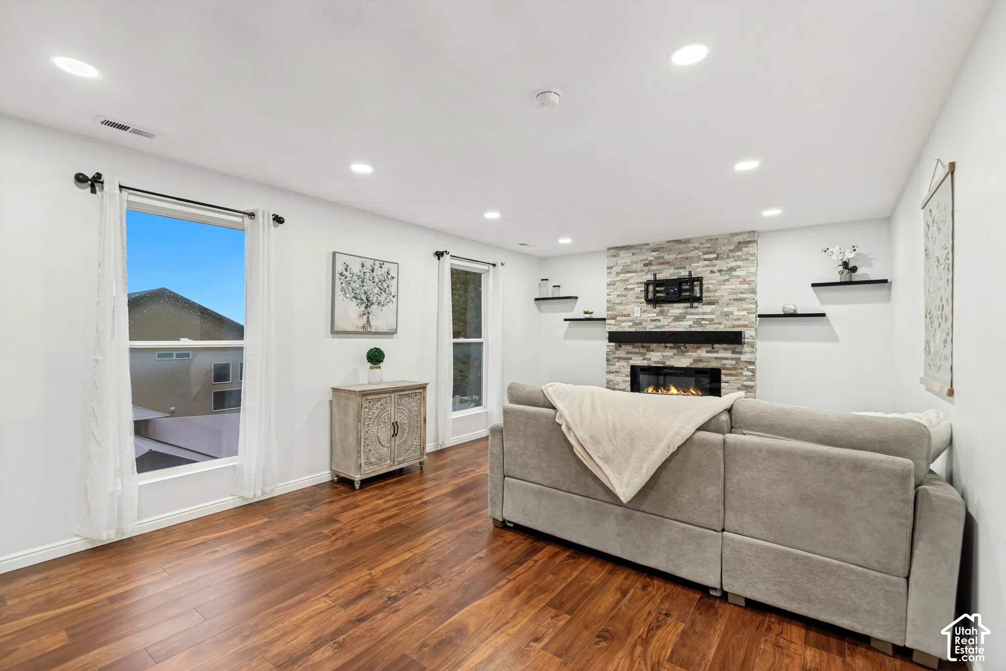 Living area featuring wood-finish flooring, recessed lighting, and a floor-to-ceiling stone-veneer fireplace with a black mantel and built-in shelving