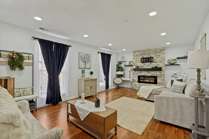 Recessed lighting, wood-finish flooring, stone-clad fireplace, built-in shelving, and multiple windows
