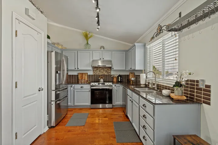 Vaulted ceiling kitchen featuring light gray cabinetry, wood-finish flooring, a stainless steel appliance suite, and a dual basin sink with a gooseneck faucet