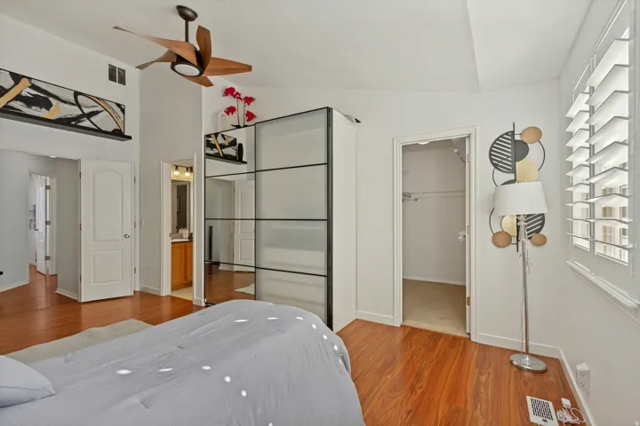 Vaulted ceiling with a ceiling fan, hardwood-finish flooring, white plantation shutters, and a frosted glass wardrobe