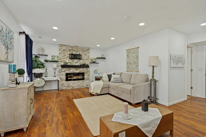 Wood-finish flooring throughout, stone-clad fireplace with built-in electric insert, recessed lighting, and wall-mounted shelving