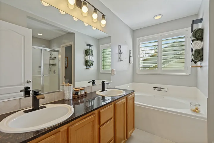 Dual sinks with dark countertops, wood-finish cabinetry, and matte black fixtures