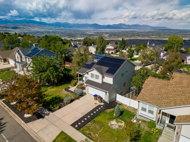 Two-story residence featuring solar panels, an attached garage, a concrete driveway, and a fenced yard with mature trees