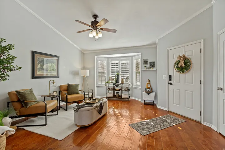 Hardwood-finish flooring, bay windows with plantation shutters, ceiling fan with light fixture, and crown molding
