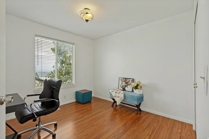 Wood-finish flooring, white walls, single window with blinds, overhead lighting fixture, and a white door with a silver-tone knob