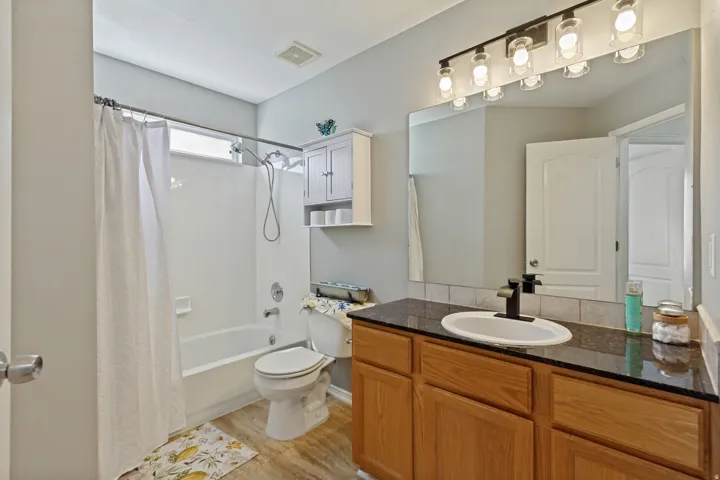 Bathroom featuring a bathtub with shower, wood-finish flooring, a vanity with a dark countertop and undermount sink, and a wall-mounted light fixture