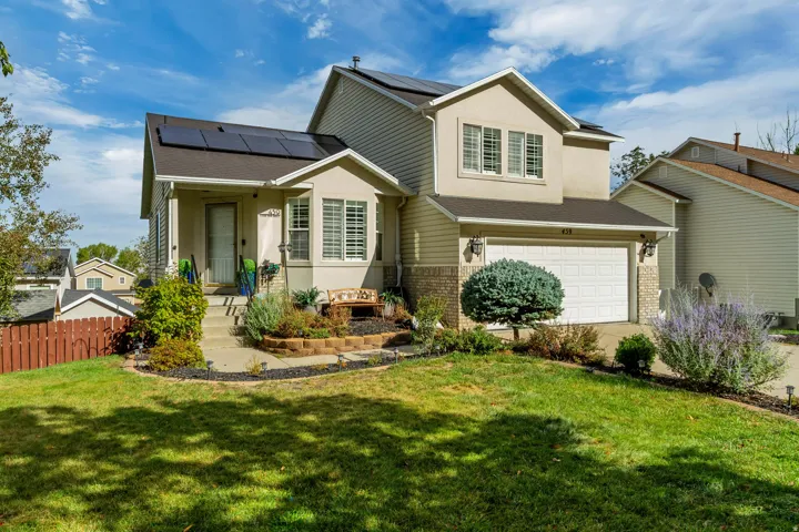 Two-story residence featuring a two-car garage, solar panels, a covered front porch, and mature landscaping