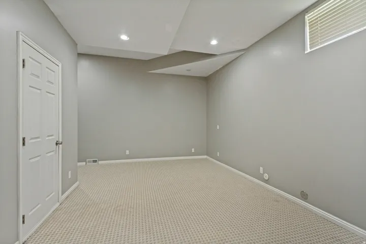 Neutral wall color, recessed lighting, patterned carpeting, white trim, and a window with blinds