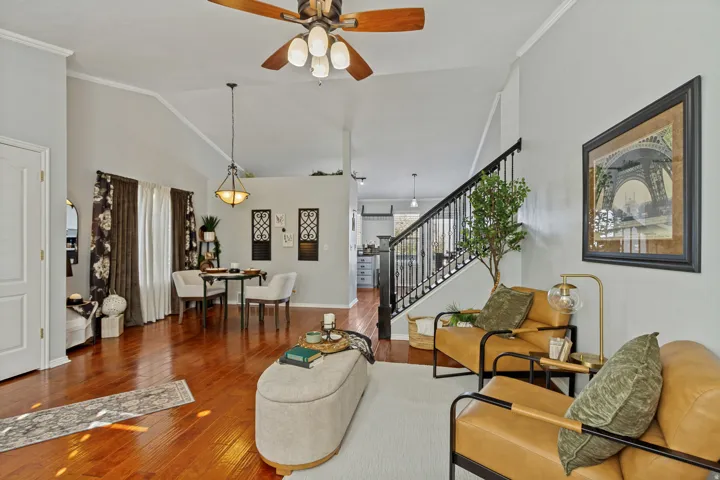 Vaulted ceilings, wood-finish flooring, staircase with wrought iron balusters, ceiling fan with light fixture, and crown molding