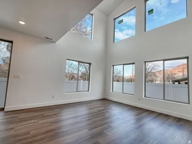 Vaulted ceiling with recessed lighting, wood-finish flooring, and multiple large windows