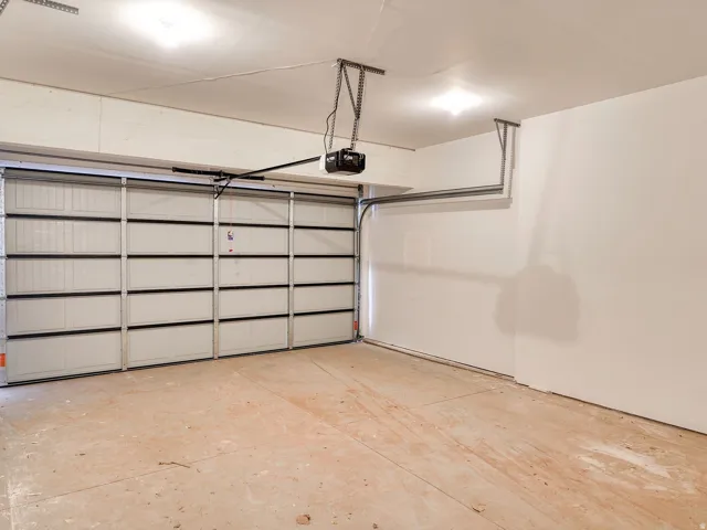 Spacious garage featuring a sectional garage door, automatic opener, concrete flooring, and ceiling-mounted lighting