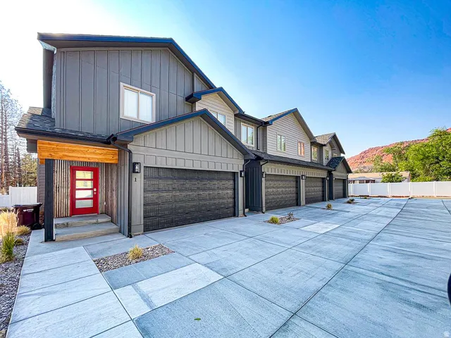 Modern exterior with vertical and horizontal siding, red paneled entry door, attached garages, concrete walkways, and a prominent mountain backdrop