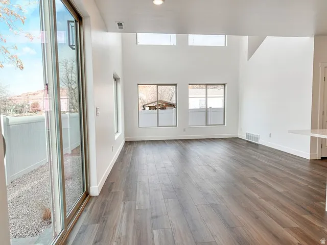 Spacious interior featuring high ceilings, wood-finish flooring, multiple windows, and a sliding glass door to an outdoor area