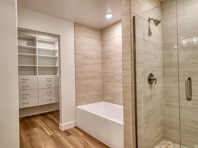 Built-in closet shelving and drawers, a soaking tub, and a walk-in shower with glass enclosure and tiled walls