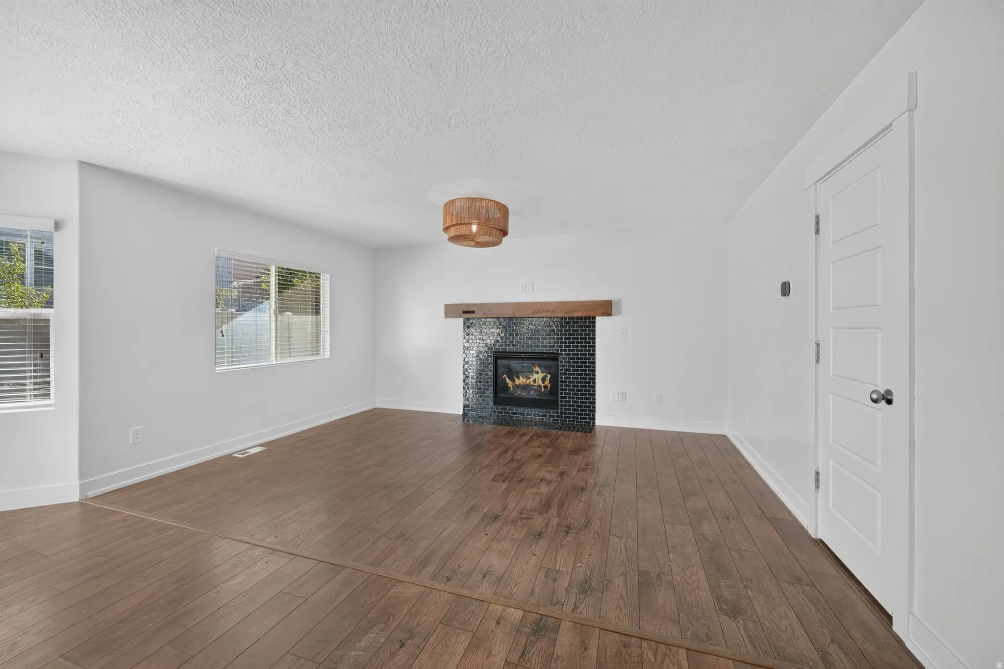 Warm wood-finish flooring, a fireplace with dark tile surround and wood mantel, white walls, and a recessed ceiling light fixture