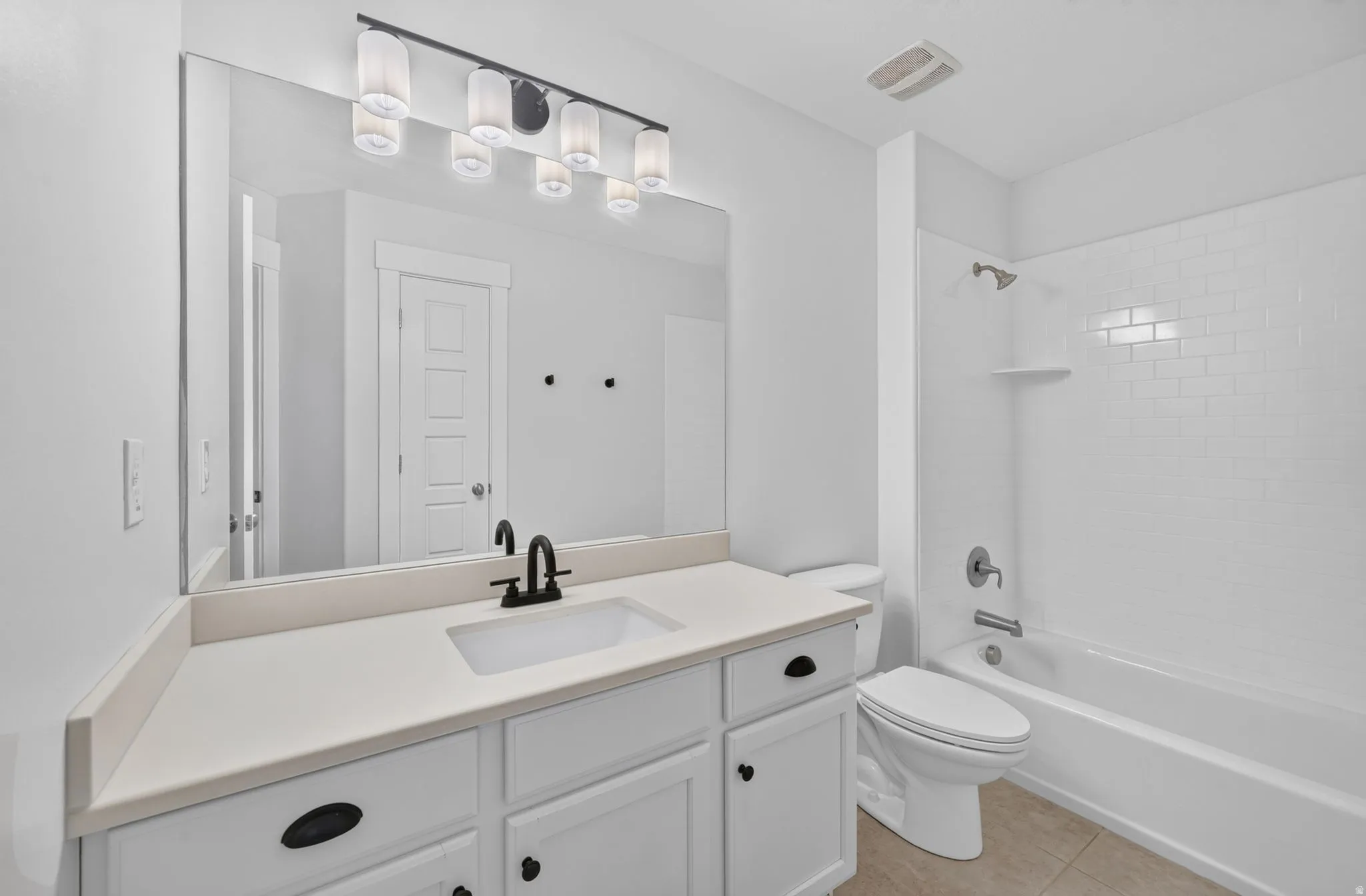 Bathroom featuring a white vanity with integrated sink, black matte faucet, a large mirror, and a white subway-tiled shower with a built-in shelf