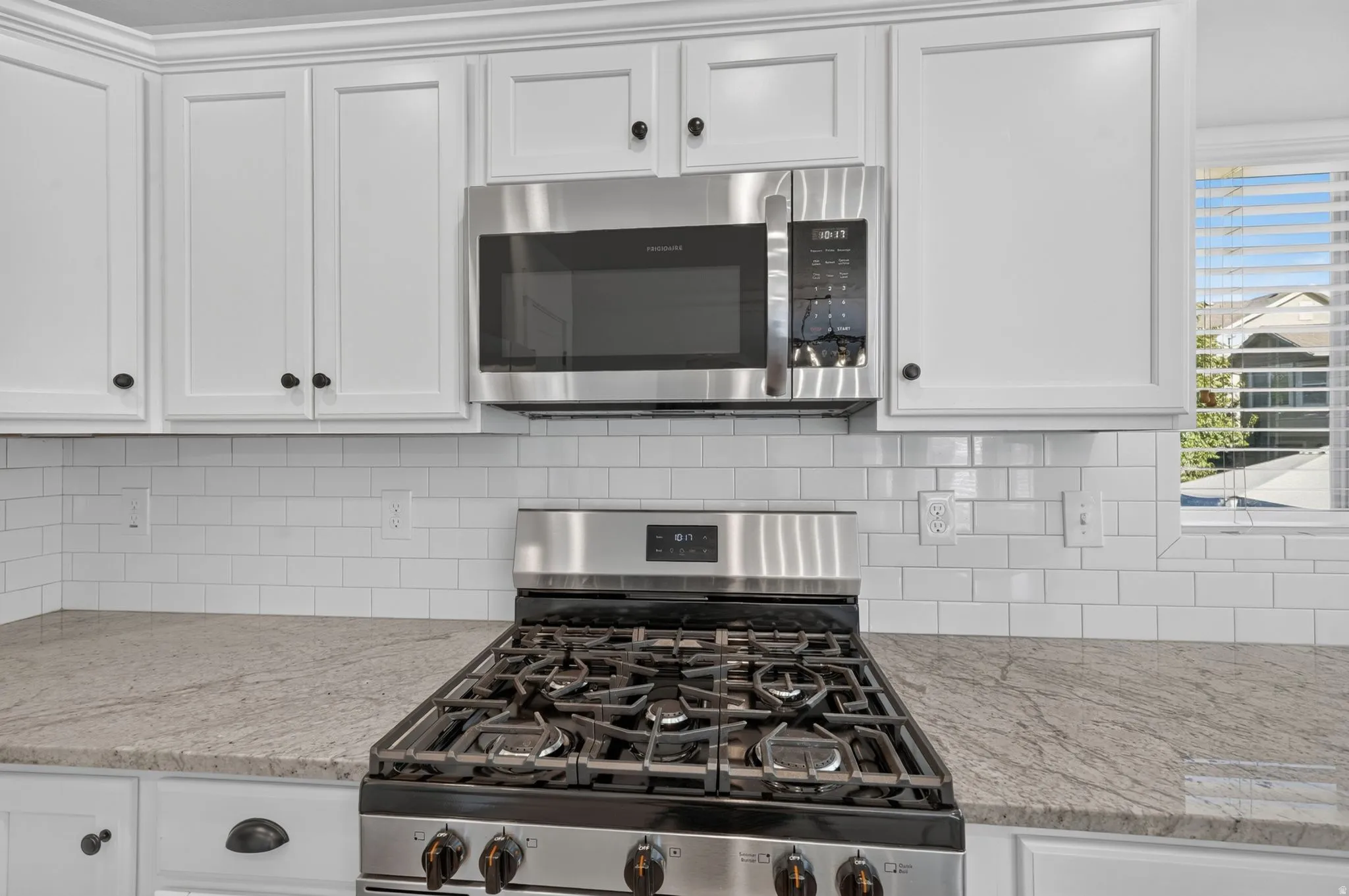 White shaker-style cabinetry, stainless steel range and microwave, light-toned countertop, and white subway tile backsplash