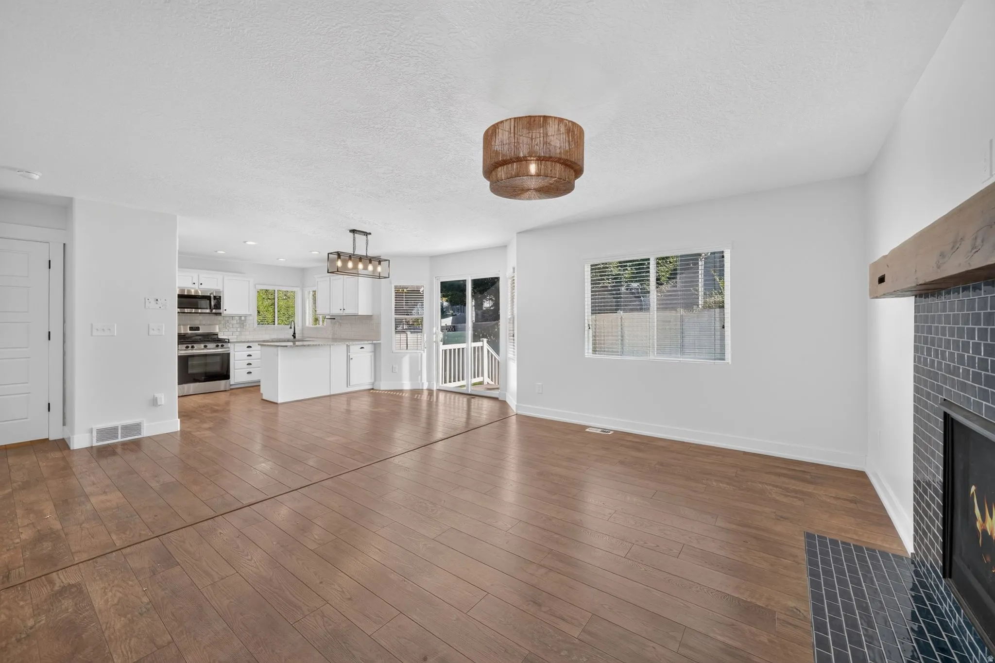 Wood-finish flooring throughout, with a drum pendant light fixture and a modern fireplace featuring a dark tile surround and a wood mantel