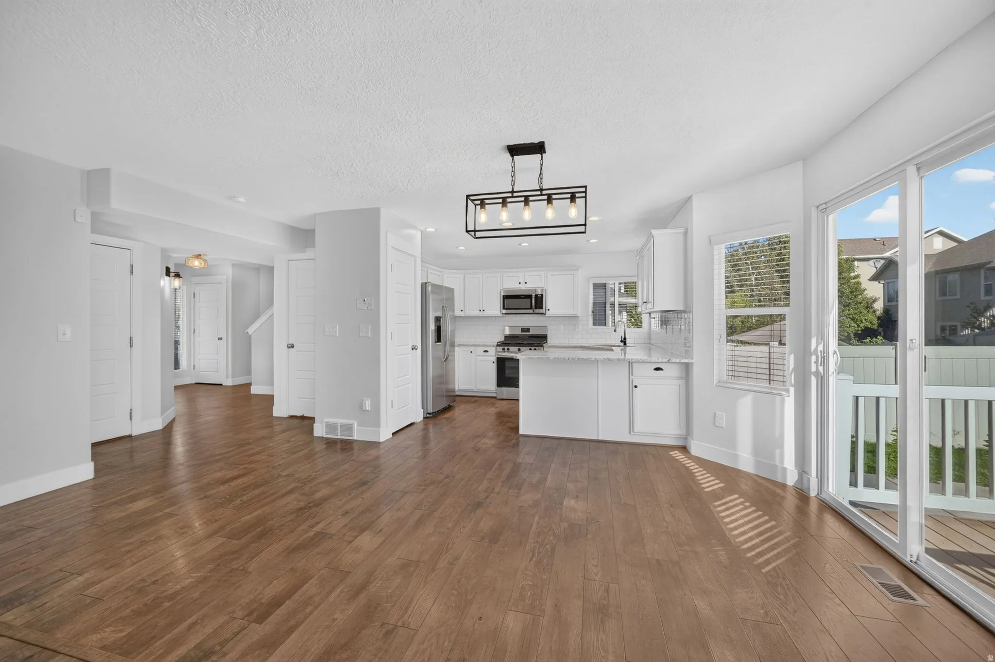 Hardwood-style flooring throughout, white kitchen cabinetry, stainless steel appliances, a kitchen island with seating, and sliding glass door access to an outdoor deck