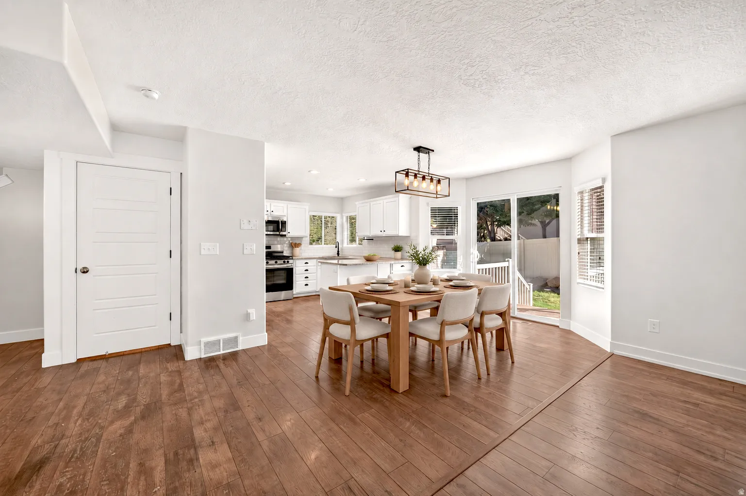 Hardwood flooring throughout, white cabinetry, stainless steel appliances, sliding glass door, and a contemporary linear chandelier