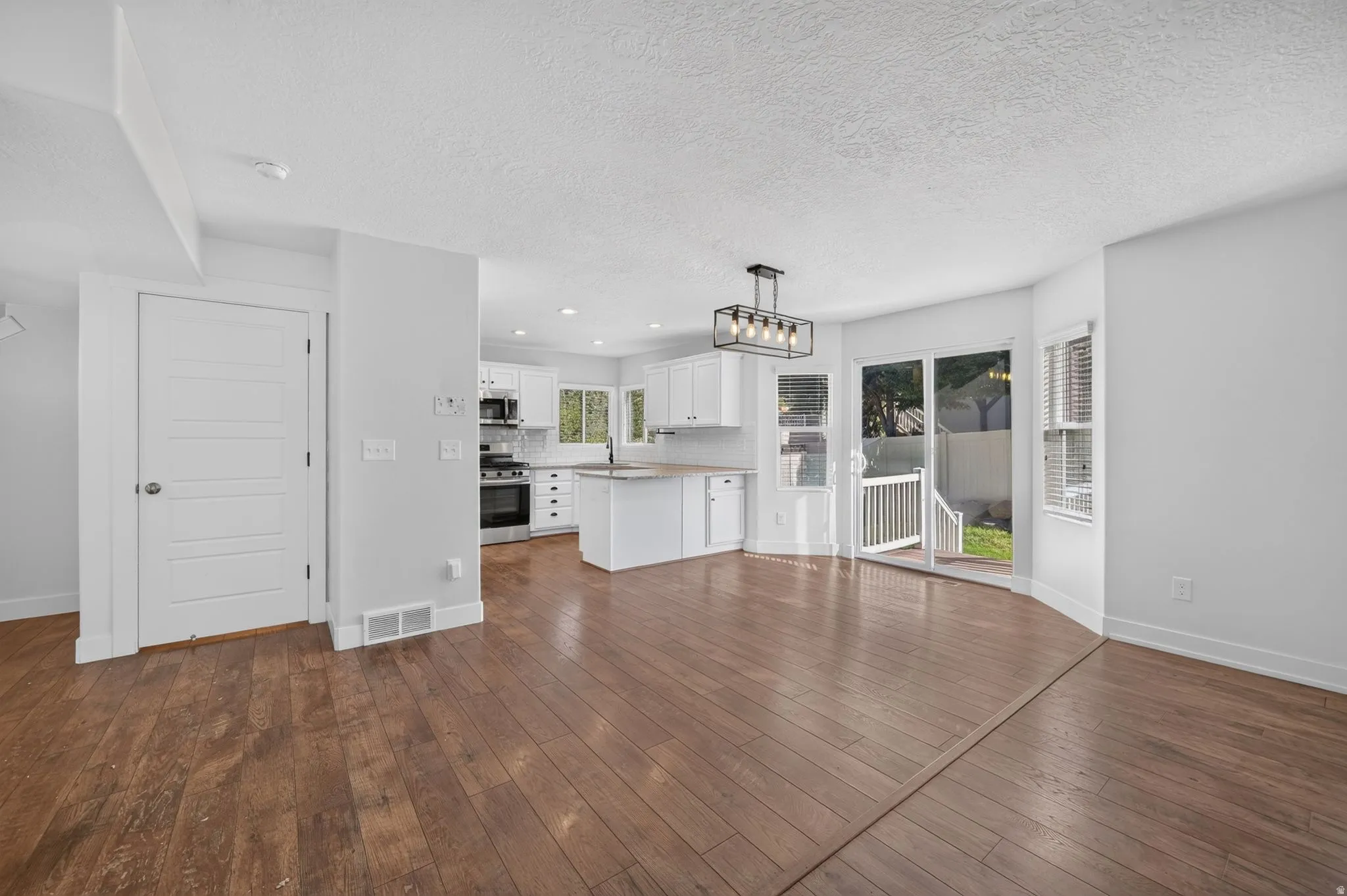Open-concept main living area featuring wood-finish flooring, white cabinetry, a kitchen island, and a sliding glass door to an outdoor area