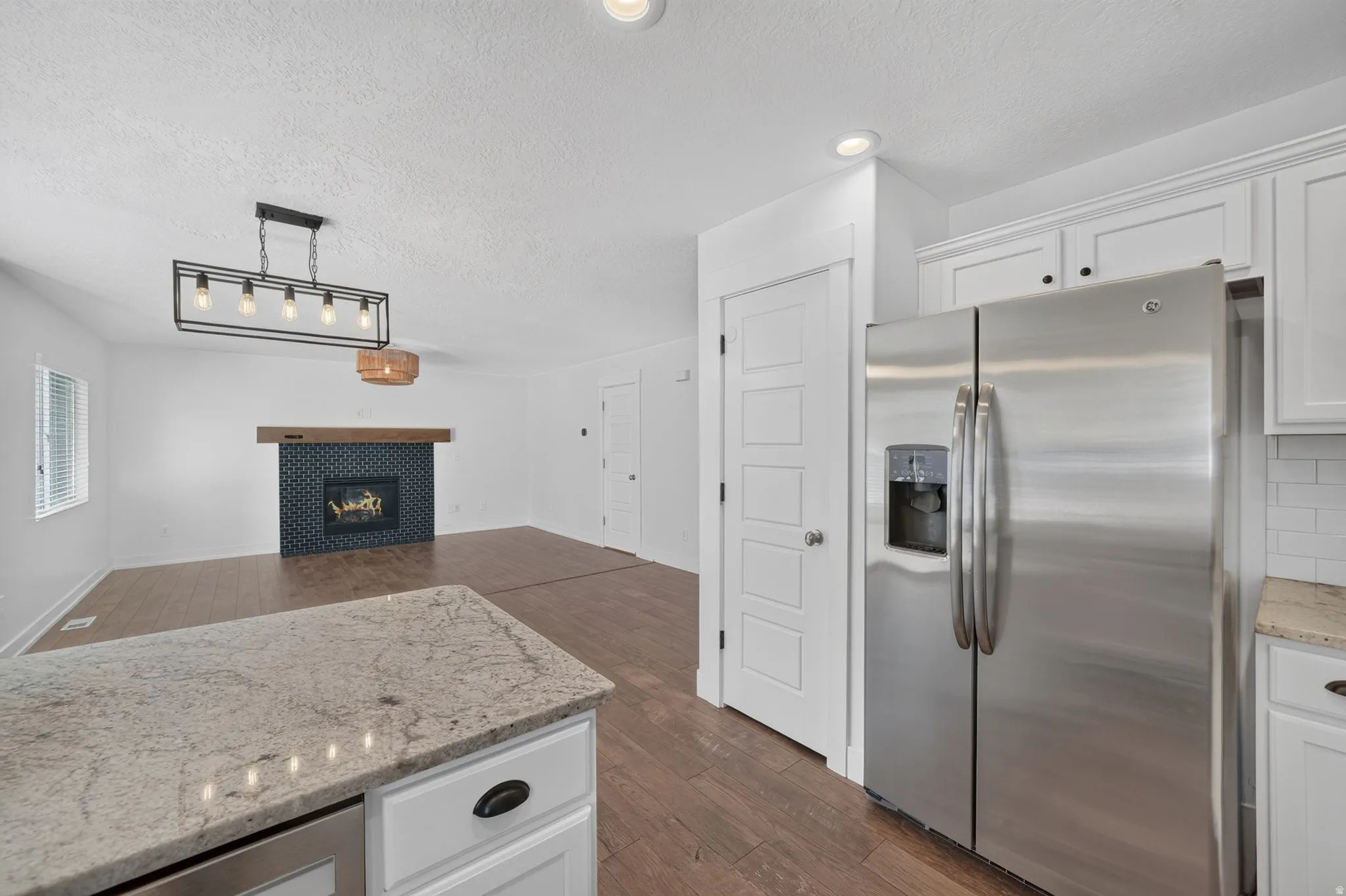 Kitchen island with a granite-style countertop, white cabinetry with dark hardware, stainless steel refrigerator, and wood-finish flooring
