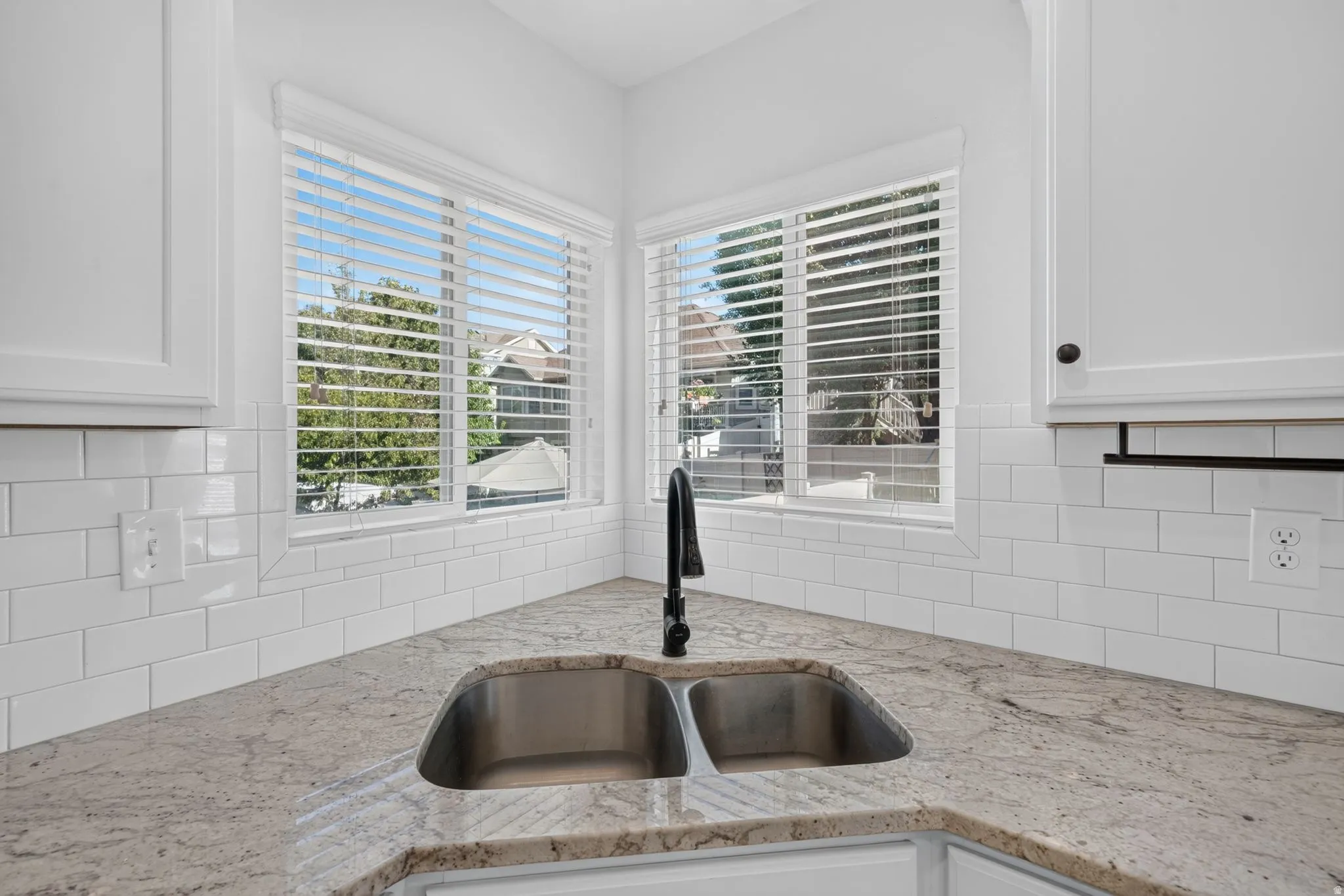 Corner stainless steel double sink with a black faucet, set into a speckled countertop