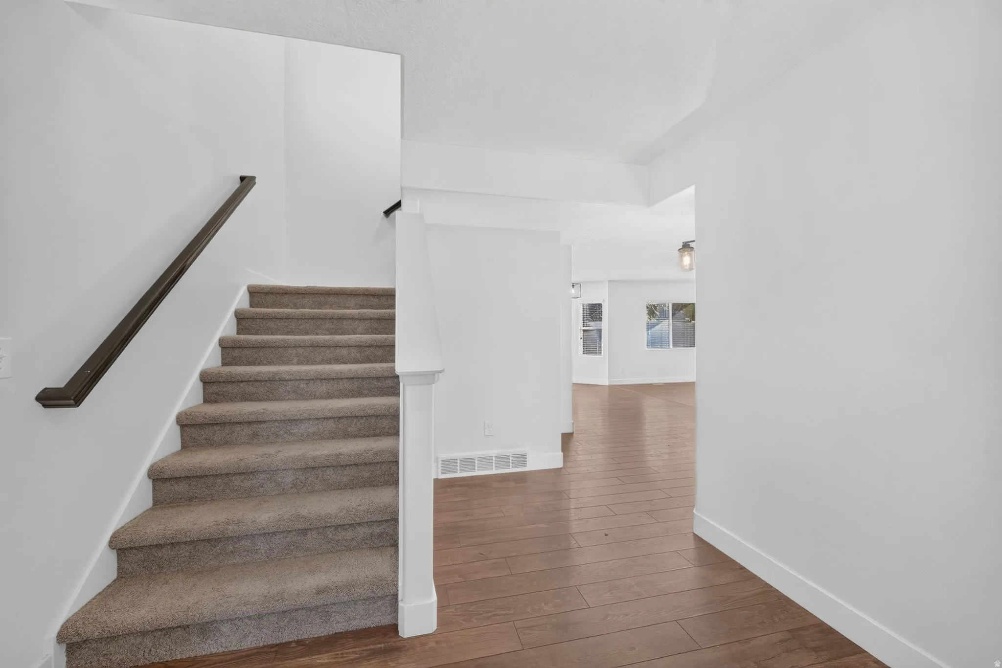 Carpeted staircase with dark wood-finish handrail, white painted walls, and wood-finish flooring
