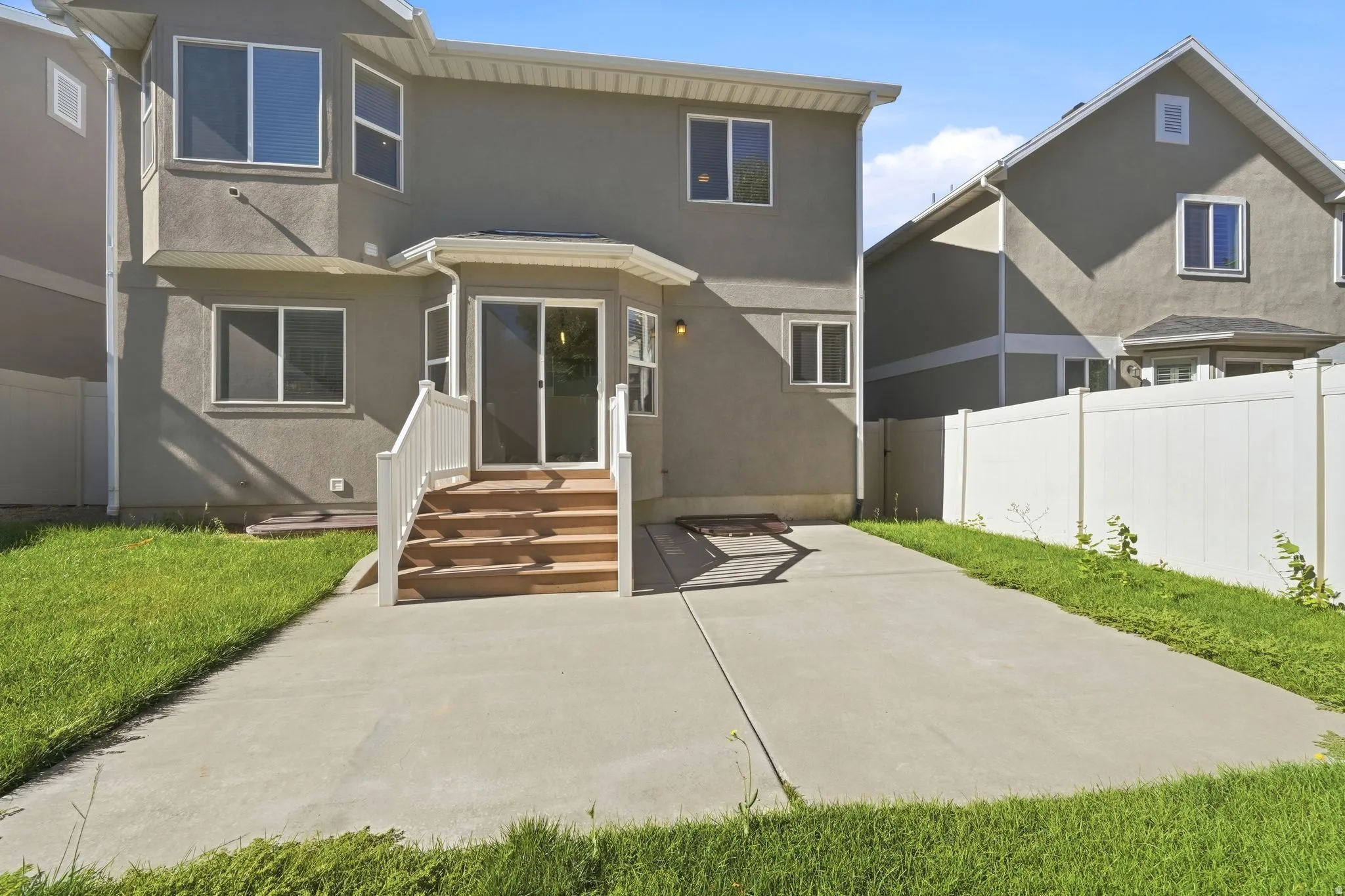 Rear exterior with a concrete patio, wooden steps, and sliding glass doors