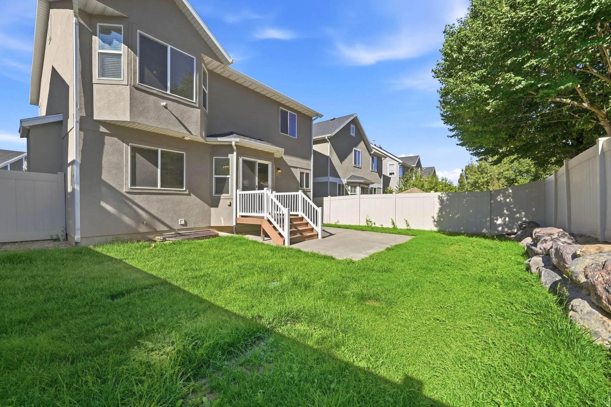 Stucco exterior with multiple windows, concrete patio, white railing, wood stairs, and a white fence
