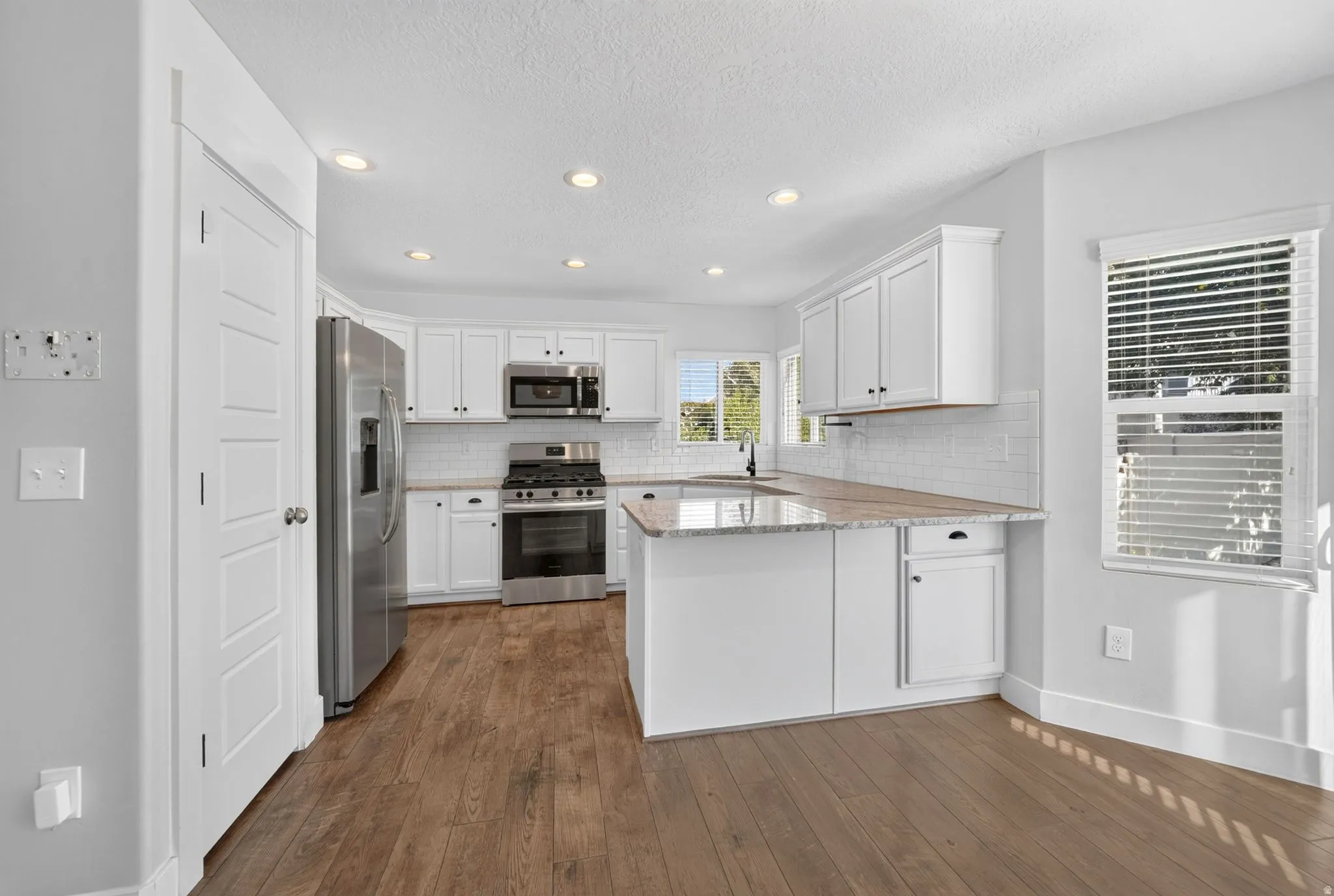 Kitchen featuring white shaker cabinetry, stainless steel appliances, wood-finish flooring, white subway tile backsplash, and recessed lighting