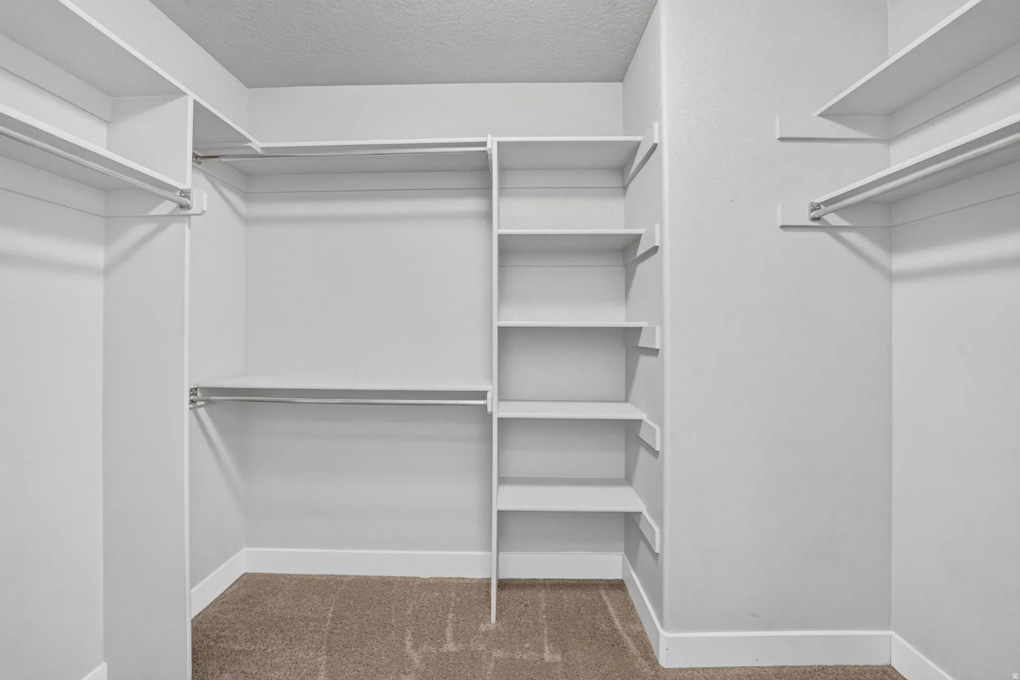 Walk-in closet featuring built-in shelving, multiple hanging rods, and neutral-toned carpeting