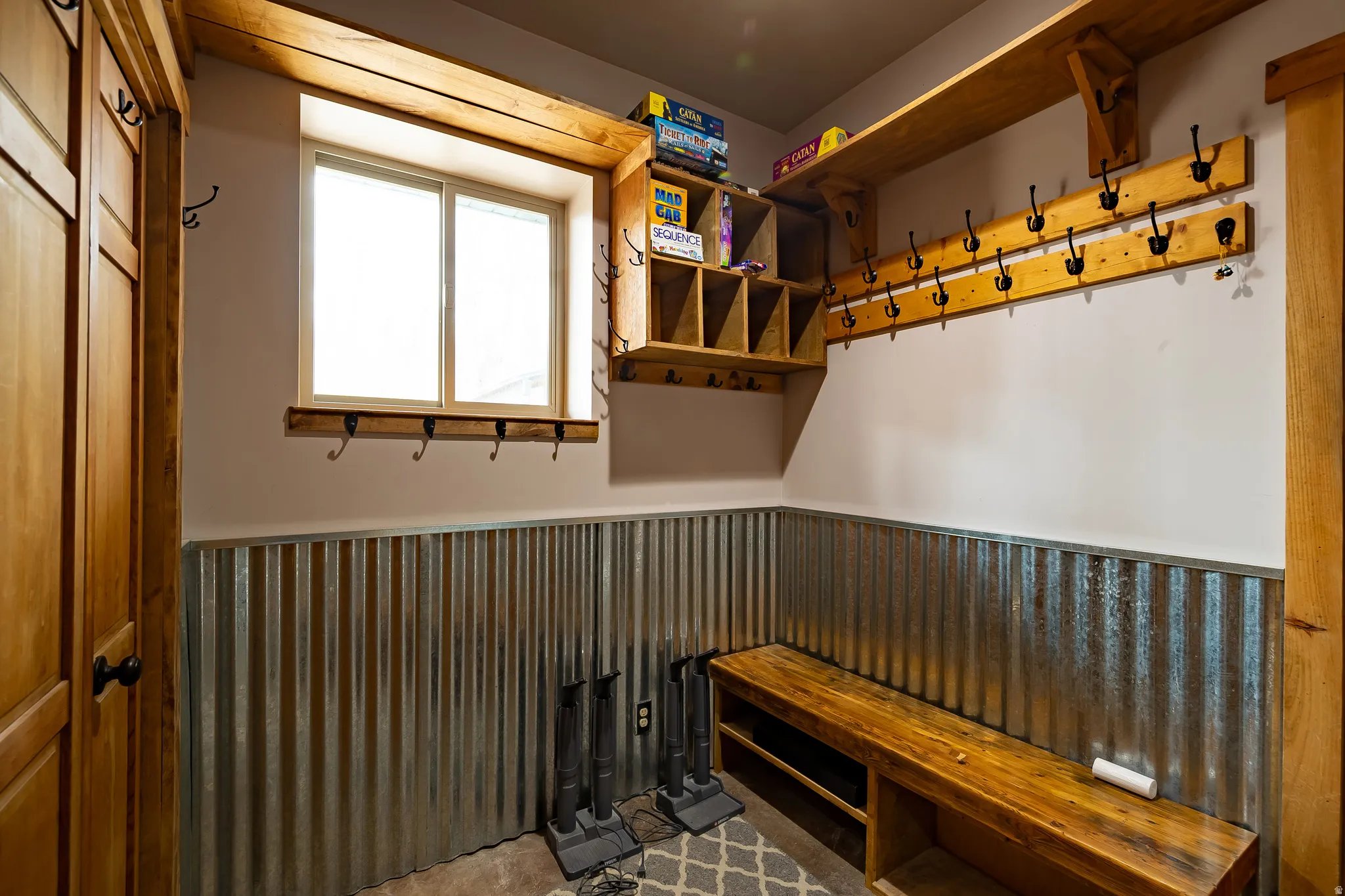 Wood-paneled door, corrugated metal wainscoting, wood bench with lower storage, wood shelving, and multiple coat hooks
