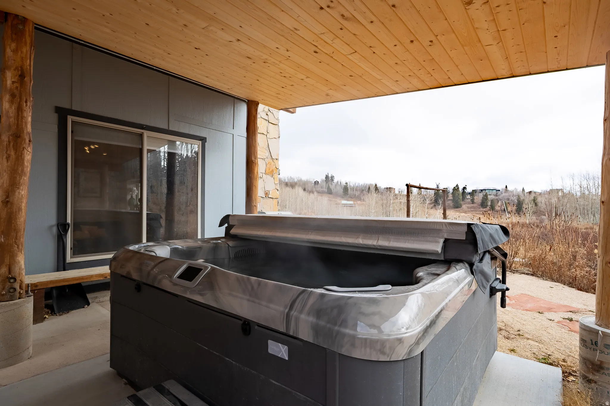 Covered patio featuring a hot tub, wood-finish ceiling, natural stone column, and sliding glass door