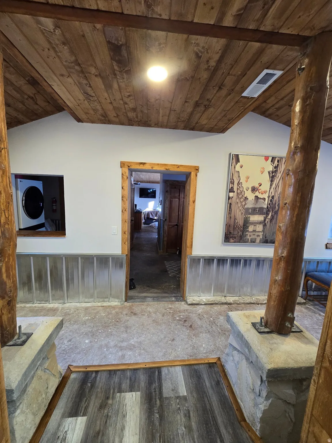 Wood-finish plank ceiling with exposed beams, stone base columns, and wood-trimmed doorways