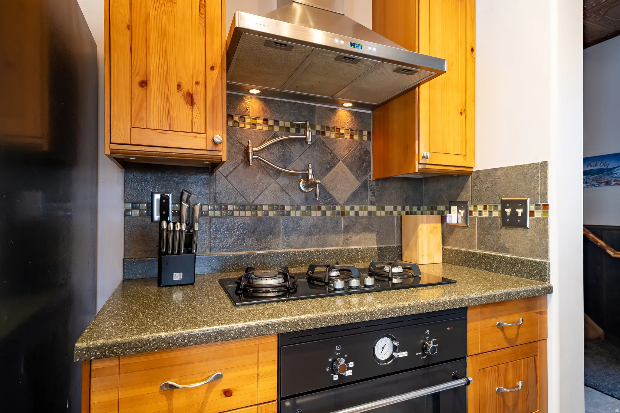 Integrated cooktop with exhaust hood, tile backsplash with decorative accents, wood cabinetry, and solid surface countertops