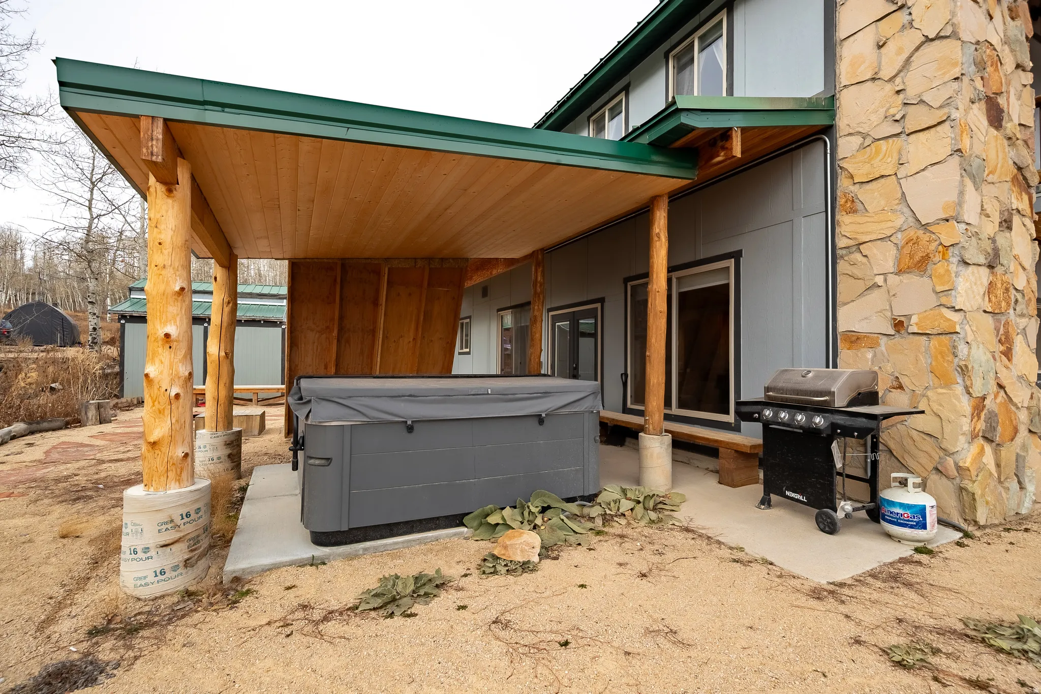 Covered patio featuring natural wood posts, wood-finish ceiling, and stone veneer siding