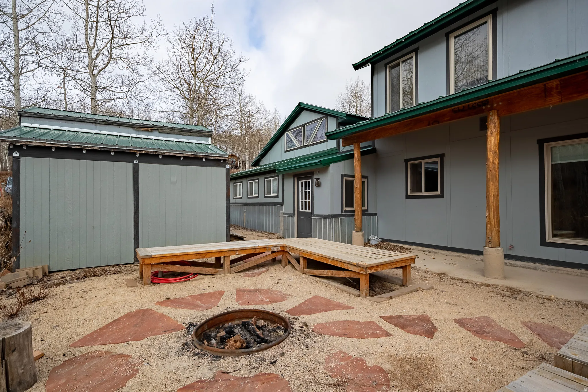 Exterior featuring a covered patio with log columns, a gravel patio area with large stone pavers, and a built-in fire pit