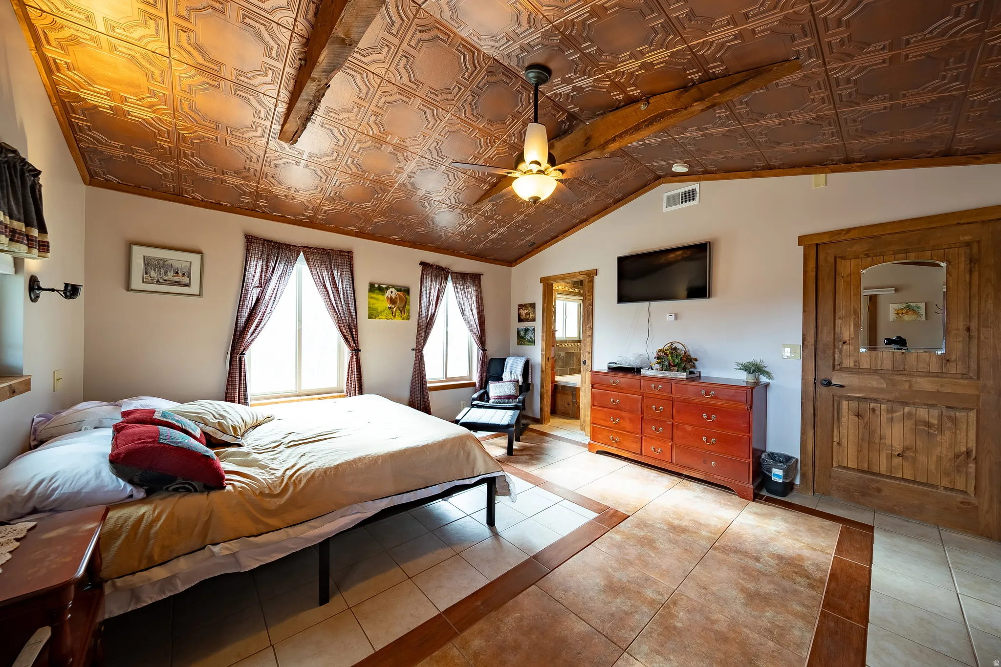 Vaulted ceiling with decorative tin tiles, exposed wood beams, ceiling fan, and tile flooring with accent border