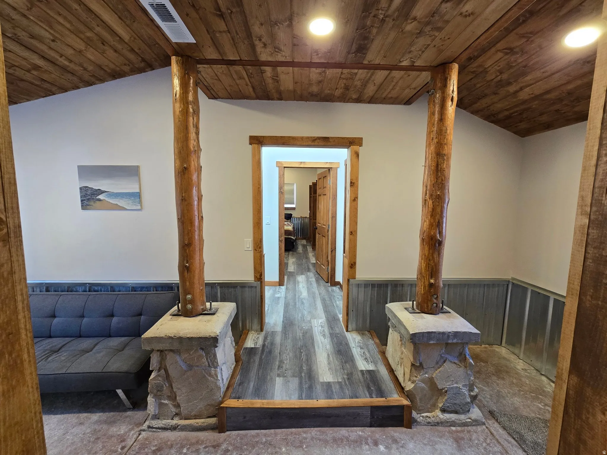 Vaulted wood-finish ceiling, exposed timber structural columns, stone-clad column bases, wood-finish flooring, and recessed lighting